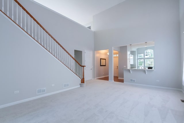 unfurnished living room featuring visible vents, stairs, and a high ceiling