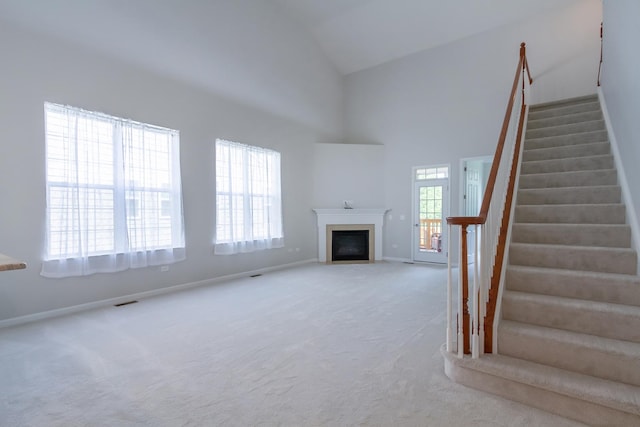 unfurnished living room with a fireplace with flush hearth, carpet floors, a high ceiling, and stairs