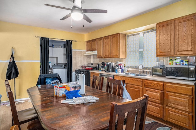 kitchen with under cabinet range hood, washer / dryer, appliances with stainless steel finishes, brown cabinets, and a sink