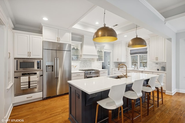 kitchen featuring a sink, custom range hood, built in appliances, white cabinetry, and light wood-type flooring