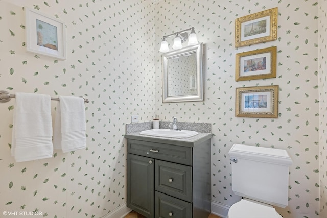 bathroom with wallpapered walls, toilet, vanity, and baseboards