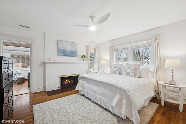 bedroom with a brick fireplace, wood finished floors, and a ceiling fan