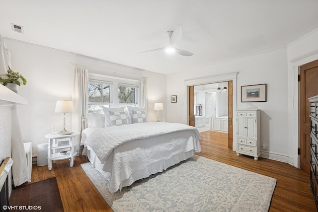 bedroom with dark wood-type flooring, a ceiling fan, ensuite bath, a fireplace, and baseboards