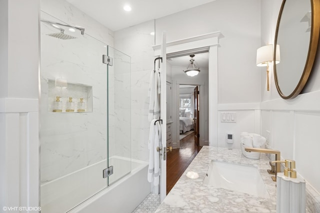 bathroom featuring combined bath / shower with glass door, wainscoting, ensuite bathroom, a decorative wall, and vanity