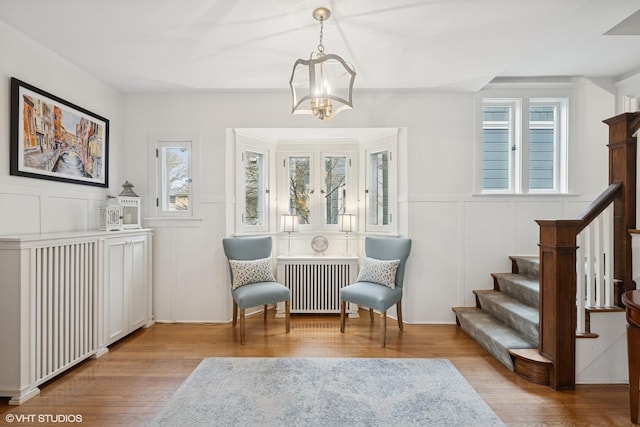 sitting room with a decorative wall, a notable chandelier, radiator heating unit, and wood finished floors