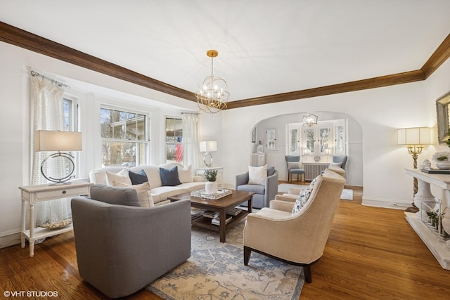 living area featuring baseboards, arched walkways, wood finished floors, and ornamental molding