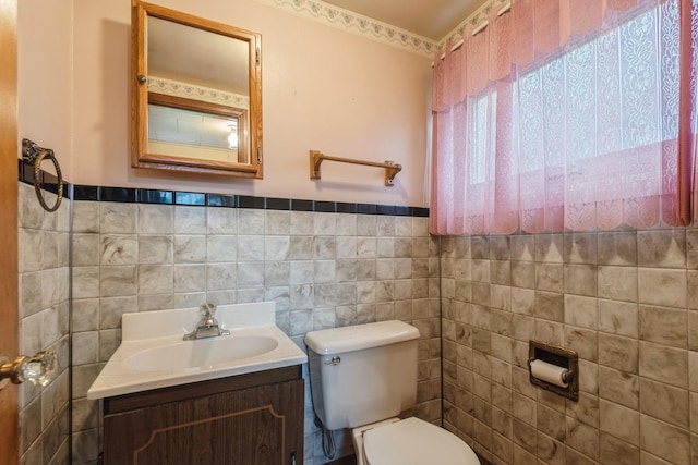 bathroom featuring toilet, tile walls, wainscoting, and vanity