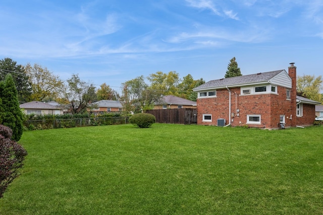 rear view of property with brick siding, a lawn, a chimney, and a fenced backyard