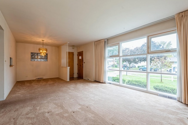 carpeted spare room with an inviting chandelier and visible vents