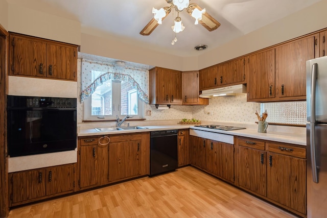 kitchen featuring brown cabinetry, a sink, black appliances, light countertops, and under cabinet range hood