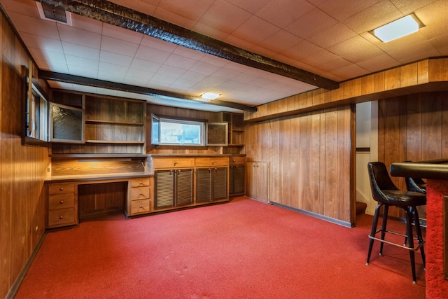 interior space with visible vents, beam ceiling, carpet, wood walls, and built in study area