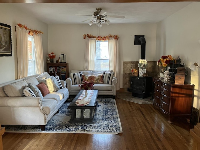 living room featuring a wood stove, a ceiling fan, and wood finished floors