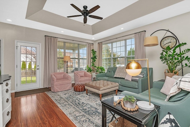 living room featuring dark wood-style flooring, ceiling fan, a healthy amount of sunlight, and a raised ceiling