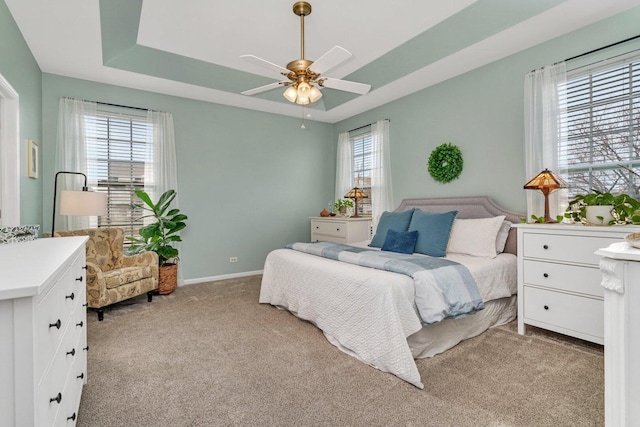bedroom featuring carpet flooring, a tray ceiling, multiple windows, and baseboards