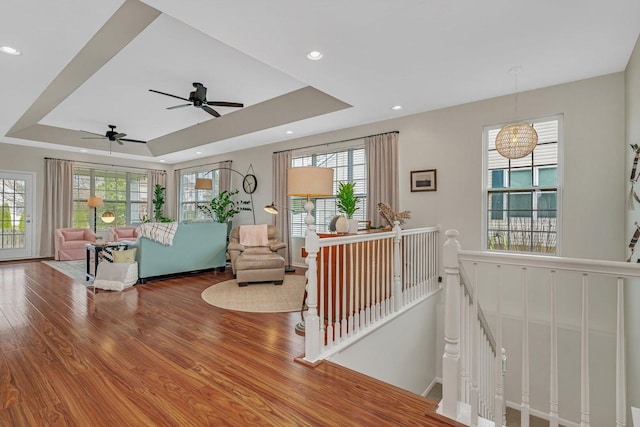 living area with a tray ceiling, wood finished floors, recessed lighting, and ceiling fan
