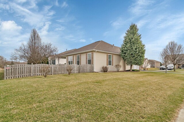 view of home's exterior featuring a shingled roof, fence, and a lawn