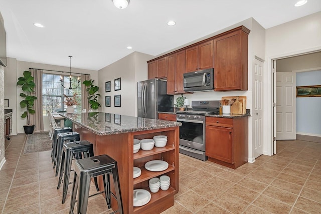 kitchen with a kitchen island, appliances with stainless steel finishes, dark stone countertops, open shelves, and a breakfast bar area