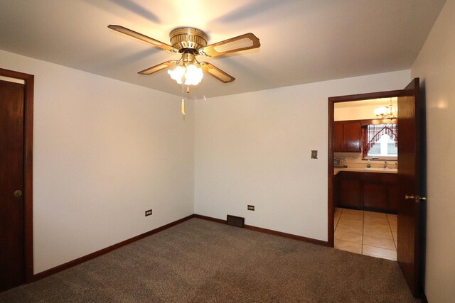 empty room with light tile patterned floors, baseboards, a sink, ceiling fan with notable chandelier, and light colored carpet