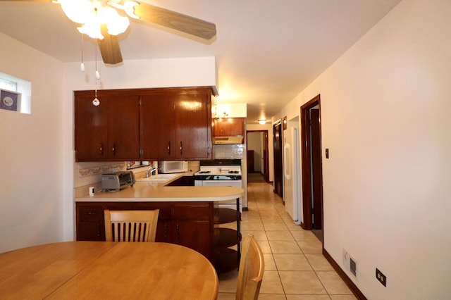 kitchen with a peninsula, white range with gas stovetop, light tile patterned flooring, under cabinet range hood, and backsplash