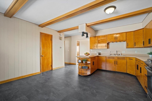 kitchen with beamed ceiling, a sink, brown cabinetry, light countertops, and baseboards