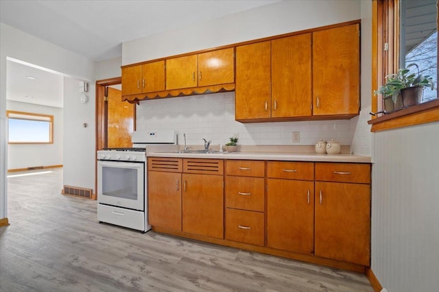 kitchen with brown cabinetry, light wood finished floors, white range with gas stovetop, a sink, and light countertops