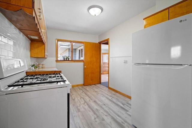 kitchen featuring a wainscoted wall, decorative backsplash, light wood-style flooring, white appliances, and a sink