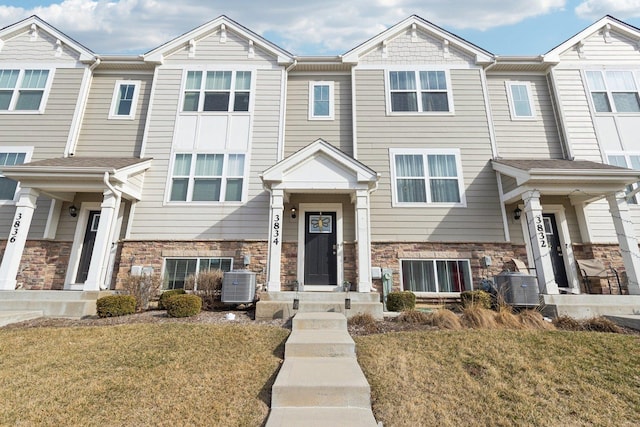 view of property with central air condition unit, stone siding, and a front yard