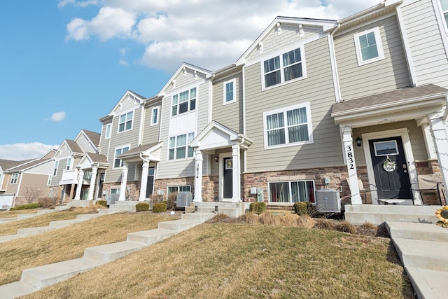 multi unit property featuring stone siding, a residential view, central AC unit, and a front yard