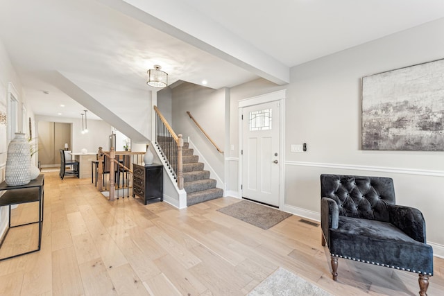 foyer entrance with visible vents, beam ceiling, baseboards, and light wood-style flooring