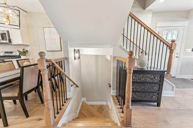 stairs featuring a notable chandelier, wood finished floors, and baseboards