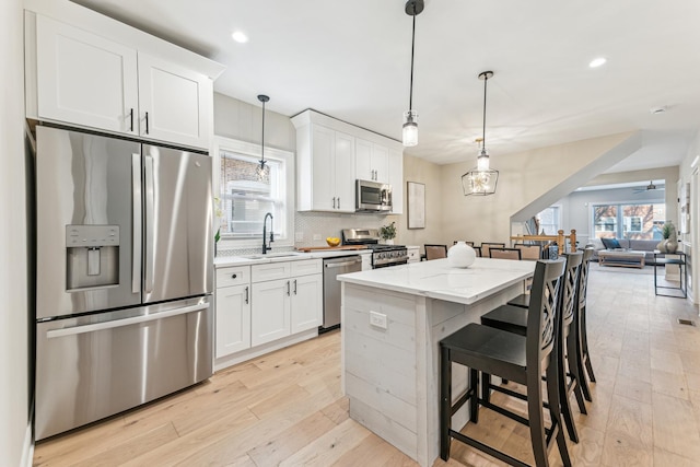 kitchen with a sink, stainless steel appliances, a kitchen island, and light wood-style flooring