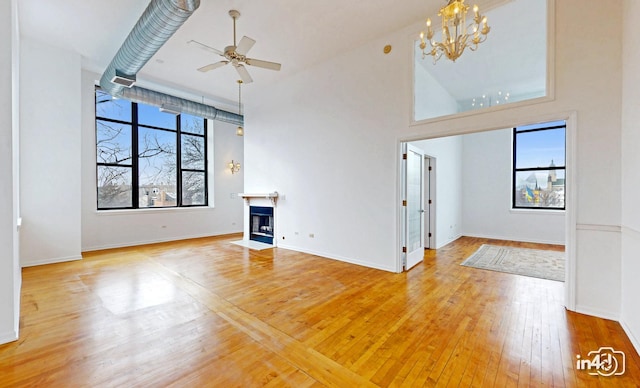 unfurnished living room featuring a fireplace with flush hearth, plenty of natural light, light wood-style flooring, and ceiling fan with notable chandelier