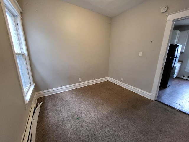 empty room with a baseboard heating unit, baseboards, and dark carpet