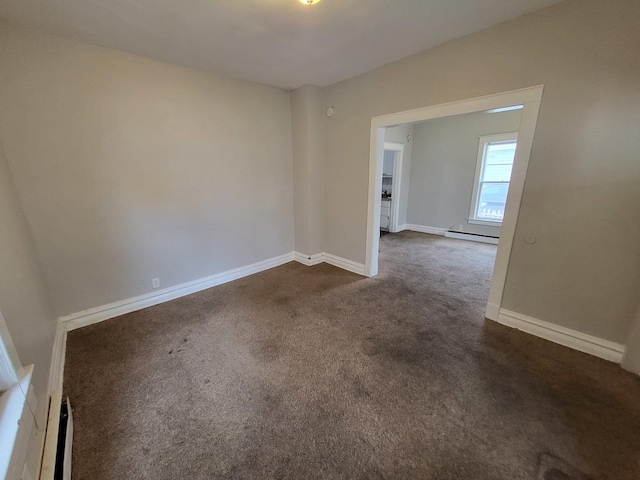 unfurnished room with a baseboard heating unit, baseboards, and dark colored carpet