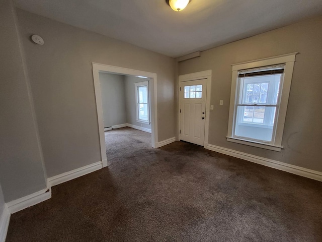 foyer entrance featuring dark carpet and baseboards