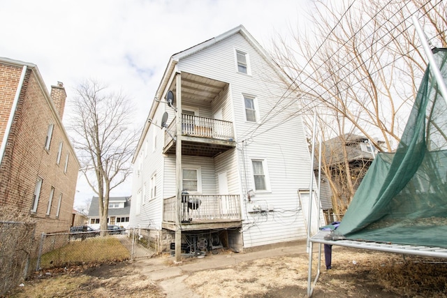 back of property featuring a balcony, a trampoline, and fence