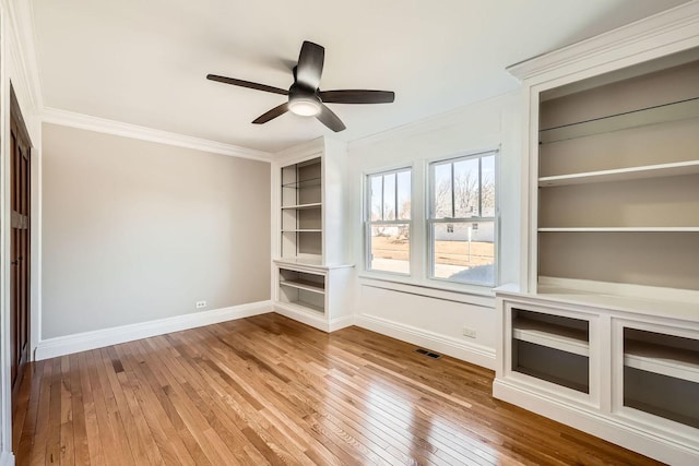 interior space featuring visible vents, ornamental molding, a ceiling fan, wood-type flooring, and baseboards