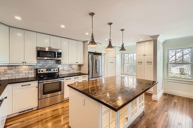 kitchen with backsplash, light wood-style floors, dark countertops, and appliances with stainless steel finishes