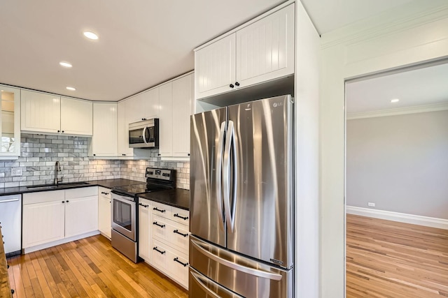 kitchen featuring dark countertops, backsplash, ornamental molding, appliances with stainless steel finishes, and a sink