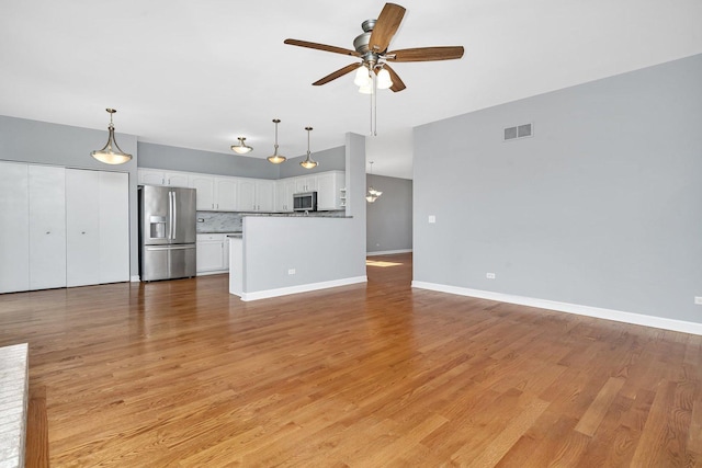 unfurnished living room featuring light wood-type flooring, visible vents, baseboards, and ceiling fan with notable chandelier