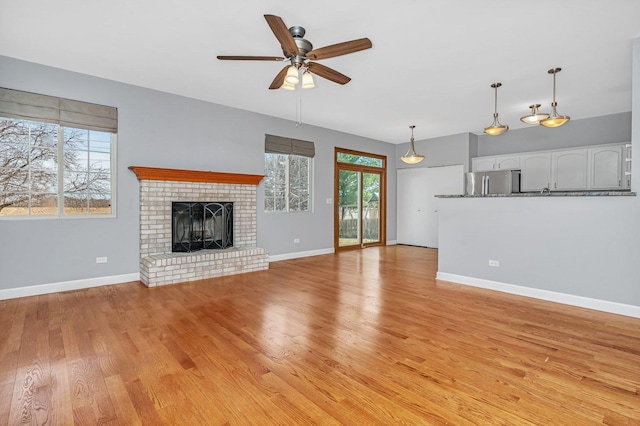 unfurnished living room with baseboards, a brick fireplace, light wood-style flooring, and a ceiling fan