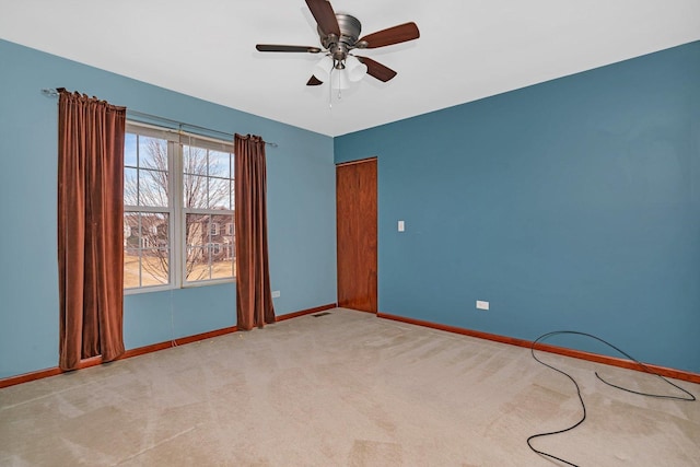 carpeted spare room with visible vents, baseboards, and ceiling fan