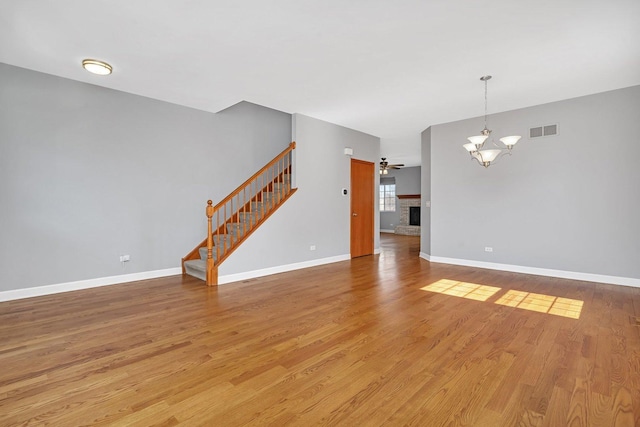 unfurnished living room with visible vents, a brick fireplace, baseboards, stairs, and light wood-style flooring