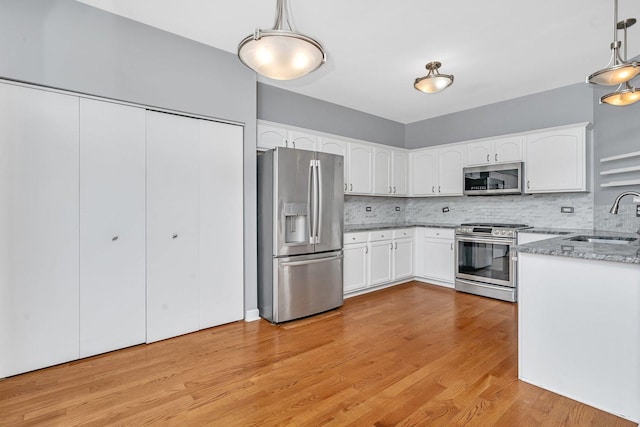 kitchen with a sink, light stone counters, tasteful backsplash, stainless steel appliances, and light wood-style floors