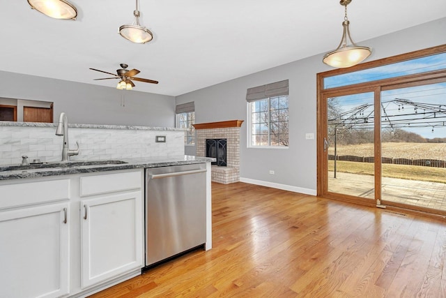 kitchen with light wood-style flooring, a sink, stainless steel dishwasher, white cabinets, and a brick fireplace