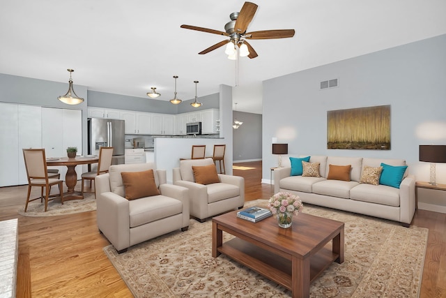 living area with visible vents, baseboards, ceiling fan, and light wood finished floors