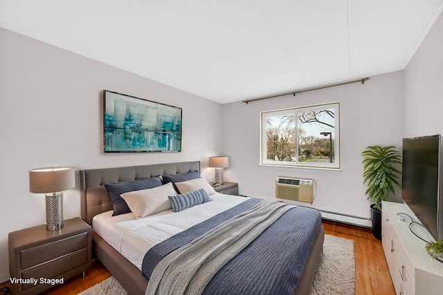 bedroom with light wood-style floors, a baseboard heating unit, and a wall mounted AC