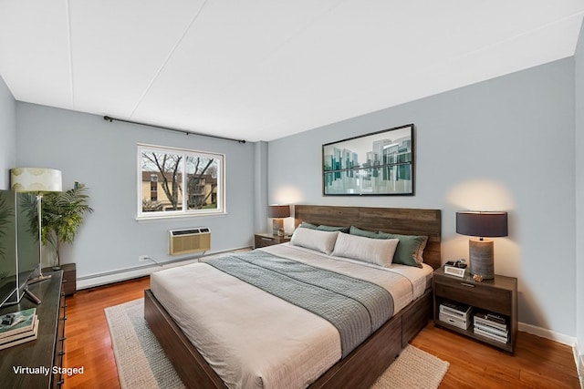 bedroom with baseboards, baseboard heating, an AC wall unit, and wood finished floors