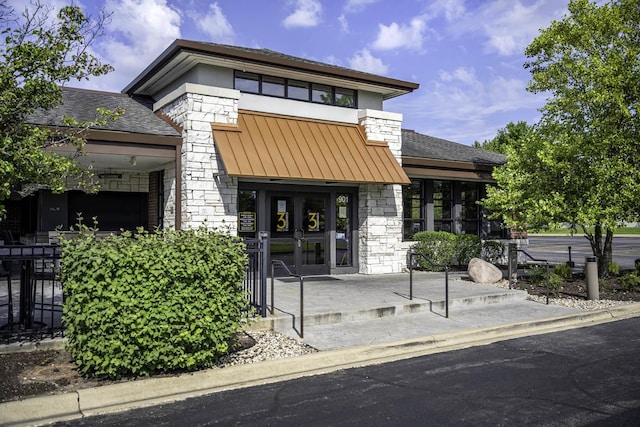 doorway to property featuring stone siding, metal roof, a standing seam roof, and a shingled roof