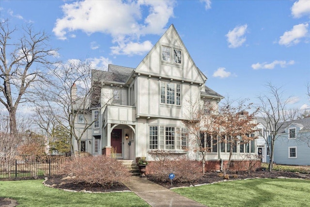 tudor home with stucco siding, a front lawn, and fence